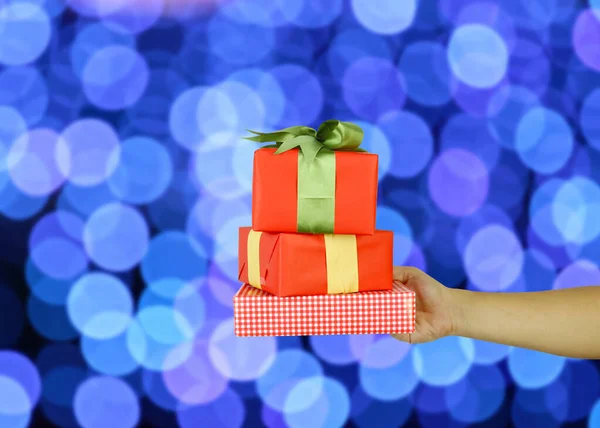 Hand of man with a red gift box on blue bokeh background. — Stockfoto