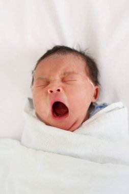 Asyalı küçük kız yatakta uyuyor ve esniyor, yeni doğan bebeğin özel bakıma ihtiyacı var..