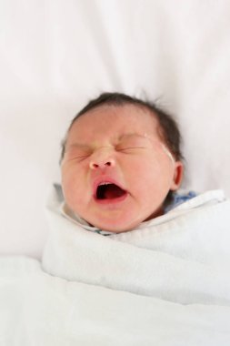 Asyalı küçük kız yatakta uyuyor ve esniyor, yeni doğan bebeğin özel bakıma ihtiyacı var..