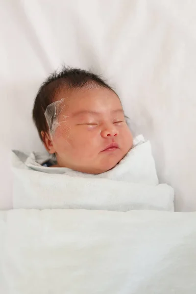 アジア系の幼児の女の子はベッドの上で寝ており 特別なケアが必要な彼女の顔 新生児を置くためのテープを持っています — ストック写真
