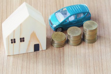 Araba ve oyuncak ev, iş fikri ve kar kavramında, tahtadan zemindeki madeni paranın yanına yerleştirilmiş..