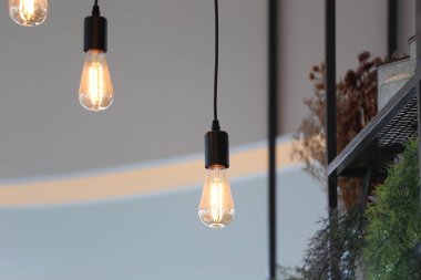 Modern bir kafeye sıcak bir ışıltı getiren, minimalist dekorlar sergileyen ve konfor ve stil için ortam sağlayan Edison ampullerini asmanın büyüleyici görüntüsü..