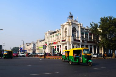 View of moving traffic at Connaught Place. Connaught Place is Delhi's busiest commercial area and houses many brands and eating outlets, You can see an auto crossing the road India, Circa 2018.  clipart