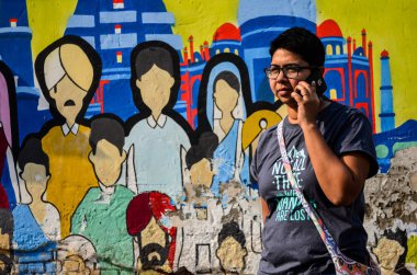 Girl talking on phone in front of a wall mural depicting various monuments and people of India in Connaught Place, Delhi, India clipart