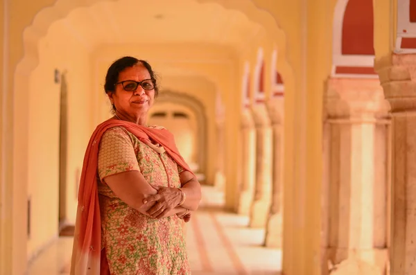 Happy looking senior Indian lady wearing traditional suit posing in the corridor of Jaipur\'s City Palace, Jaipur, Rajasthan, India