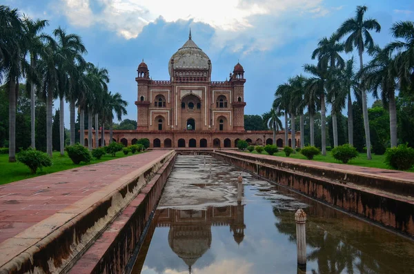 Safdarjung Tomb against the blue sky looking majestic between palm trees. Shot on a day with blue sky & beautiful warm sunlight. Reflection at the fountains & gardens make this a great tourist spot