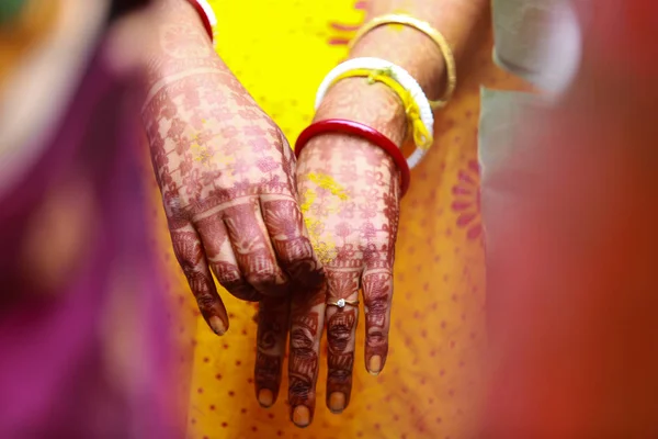 Hands of a Bengali bride showing her henna tattoo - mehendi, saakha, polla (red and white bangles) and wedding ring against her yellow red saree in the background in Kolkata, Delhi, India