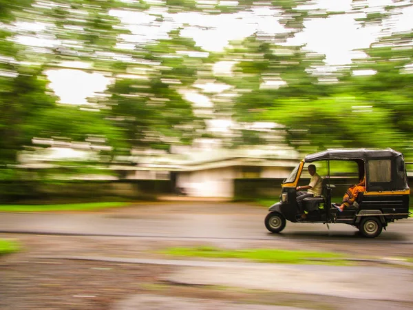 Auto rickshaws are a popular mode of transportation in India for last mile travel. The photograph shows the panned shot of an Auto speeding against trees in the background in Delhi, India