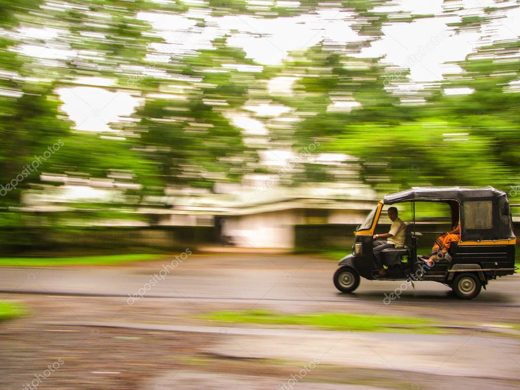 Auto rickshaws are a popular mode of transportation in India for last mile travel. The photograph shows the panned shot of an Auto speeding against trees in the background in Delhi, India
