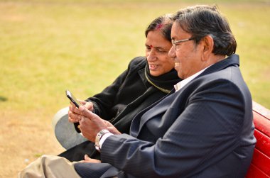 Cep telefonunuzda çalışma ve konuşurken, gülümseyen, Delhi, Hindistan bir parkta gülüyor üst düzey çift