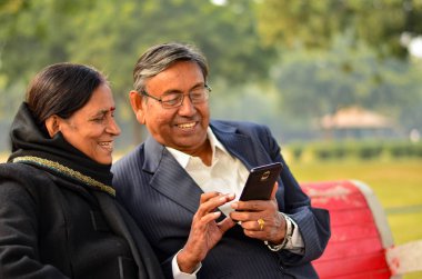 Cep telefonunuzda çalışma ve konuşurken, gülümseyerek, bir parkta Delhi, Hindistan kışları gülüyor üst düzey çift
