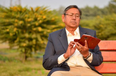 Delhi, Hindistan bir parkta kırmızı bir bankta otururken telefonunu kontrol üst düzey Hintli