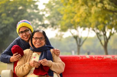 Delhi, Hindistan bir parkta kırmızı bir bankta oturan mutlu görünümlü genç Kızılderili kadın onun annesi örgü kazak