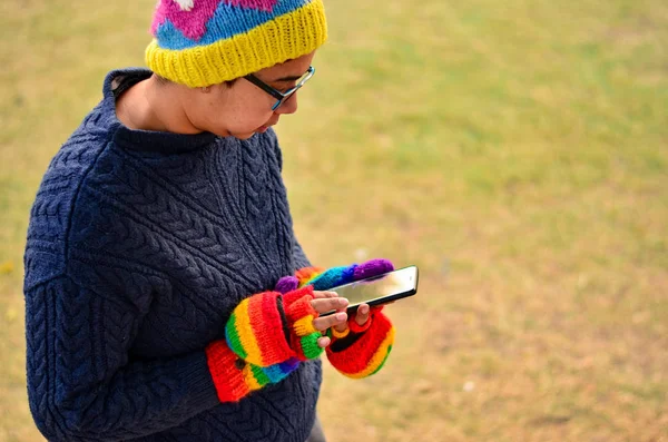 Woman wearing colorful mittens and cap operating phone in winters in a park in Delhi, India