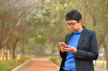 Telefonunu ayar siyah bir iş giyen / resmi bir açık uygun kontrol kendine güvenen genç bir Hint kurumsal profesyonel kadın kısa saçlı closeup portresi 