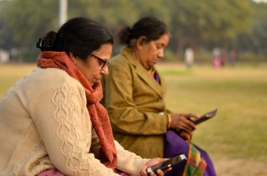 Delhi, Hindistan açık bir parkta onların smartphone üzerinde Kuzey ve güneyde Hint kıdemli yaşlı kadınlar teknolojisini kullanarak kışlar sırasında meşgul.
