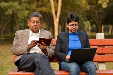 Bir telefon ve Batı partilerimiz hworking üstünde a laptop Delhi, Hindistan bir parkta genç bir Hintli kadın üzerinde çalışan bir tüvit ceket giyen bir üst düzey Hintli, yakın çekim