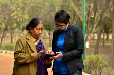 Delhi, Hindistan bir parkta bir cep telefonu kullanarak eski üst düzey kadın rehberlik genç Hintli kadın