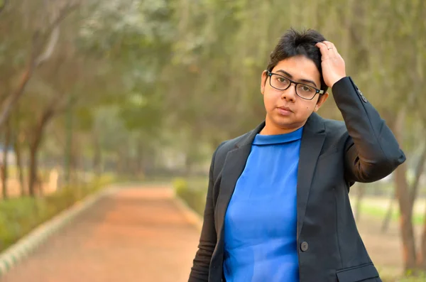 Young confident Indian professional woman wearing western business attire running fingers through her short hair in an outdoor setting wearing a black business / formal suit with a blue top
