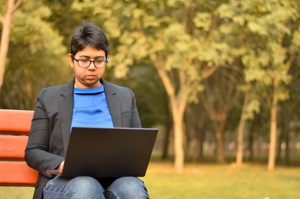 Confident Indian professional business woman in business attire working on a laptop on a park bench