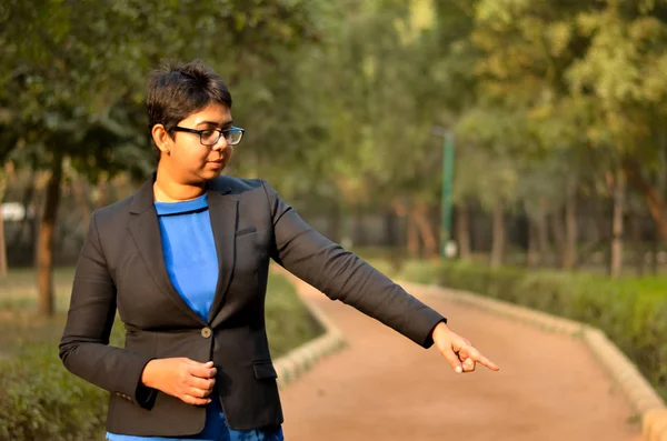 Young Indian woman working business professional pointing left down in a formal corporate business suit in an outdoor location