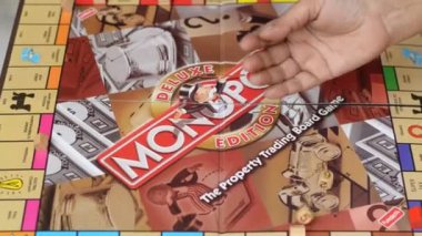 London, England, UK, 2019. Player Rolling dice on a Monopoly board. Monopoly has become a part of popular world culture, it's locally licensed used as a fun financial educational game worldwide