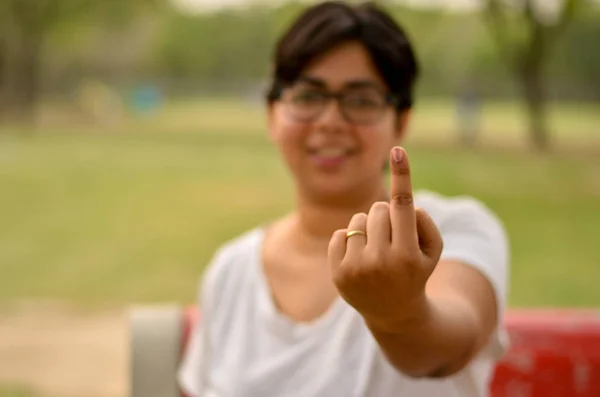 Young Indian woman sitting on the red bench in a park and showing their inked finger after casting their vote in election in Delhi, India