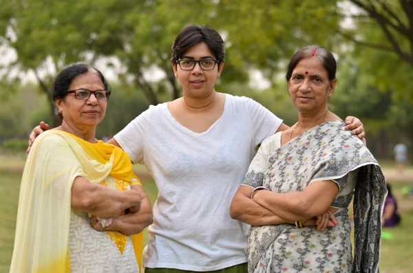 Portrait of two senior Indian women  women standing with their daughter / daughter-in-law in a park wearing saree and salwar kamiz with crossed hands during winters in Delhi, India