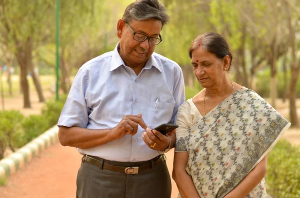 Senior couple in park looking at  their smart phone and laughing in Delhi, India