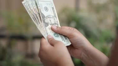 Amerika Birleşik Devletleri Doları (USD) 100 $ve 20 $'lık banknotları sayan eller dışarıda yeşil bokeh arka planda. ABD (ABD) için ABD para birimidir.)