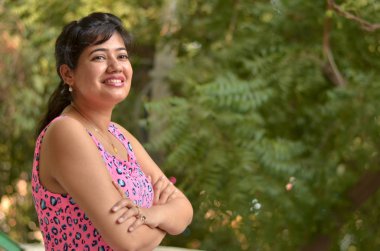Yeni Delhi, Hindistan 'da bir parkta elleri çapraz duran pembe elbiseli genç bir kadın modelin portresi.