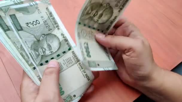Hände, die neue 500-Rupien-Scheine in indischer Währung vor einem hölzernen Bokeh-Hintergrund zählen. Ein zerrissener Zettel wird im Bündel gefunden und getrennt — Stockvideo