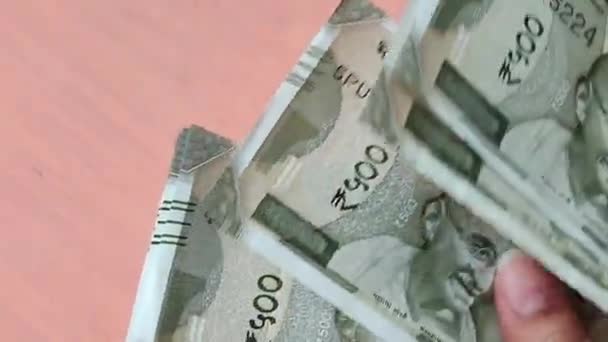 Hände, die neue 500-Rupien-Scheine in indischer Währung vor einem hölzernen Bokeh-Hintergrund zählen. Ein zerrissener Zettel wird im Bündel gefunden und getrennt — Stockvideo