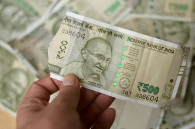 500 Rupi 'lik yırtık bir Hint parası tutan bir kadın. Mahatma Gandhi' nin sahte bir arkaplanda 500 Rupluk banknot bastırdığını gösteriyor.