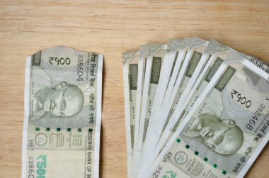 Yırtık yeni bir Rupi 500 Rupi Hint kuruşu banknotları ahşap bir bokeh arka planına karşı bir destenin yanında tutulur..