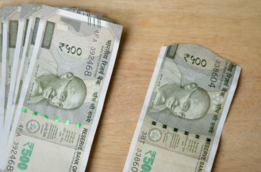 Yırtık yeni bir Rupi 500 Rupi, ahşap bir arka planda, çıtır çıtır bir banknotun yanında saklanıyor..