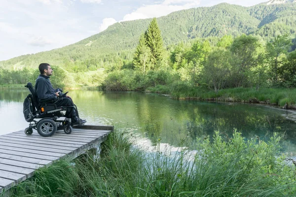 Hombre en silla de ruedas sosteniendo la cámara sin espejo cerca del lago en la naturaleza — Foto de Stock