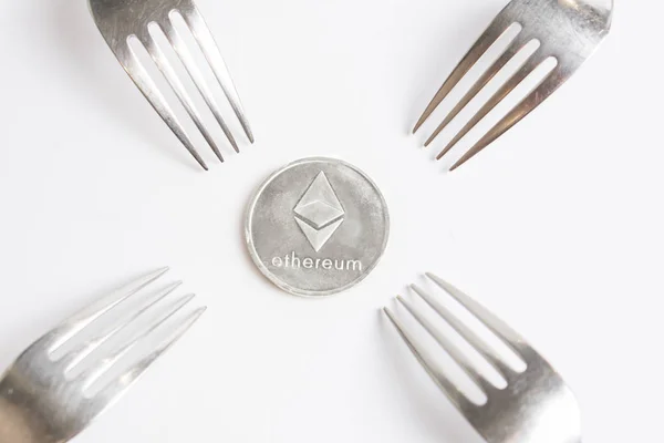 Ethereum cryptocurreny moneda de plata colocada entre horquillas sobre fondo blanco, tenedor duro — Foto de Stock