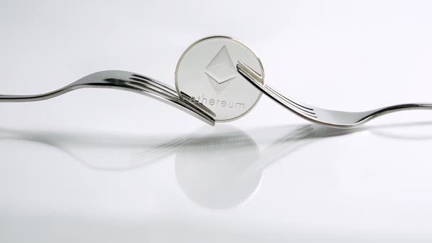 Slide zoom in shot of Ethereum fork concept with Ethereum coin and two forks on the white background with reflection — Stock Video