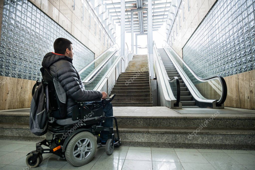 Rear View Of A Disabled Man On Wheelchair In Front Of escalator and staircase with copy space