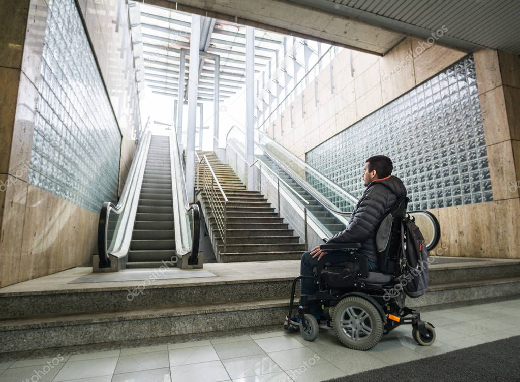 Rear View Of A Disabled Man On Wheelchair In Front Of escalator and staircase with copy space