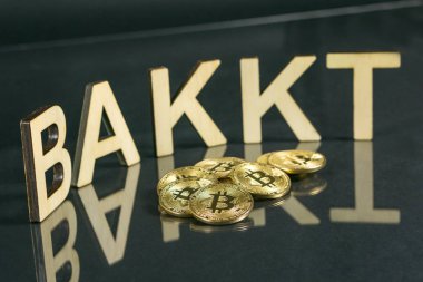 Bitcoin coins in front of bakkt sign made of wood with reflection on the table, Slovenia - December 27th clipart