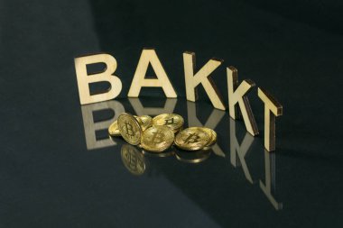 Bitcoin coins in front of bakkt sign made of wood with reflection on the table, Slovenia - December 27th clipart