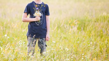 Genç çocuk bir buket çiçek çayırda bir güneşli havalarda günde annesi için toplama.