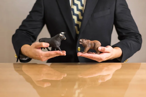 Young businessman trader holding in hands bear and bull figures. Bullish and Bearish market concept.