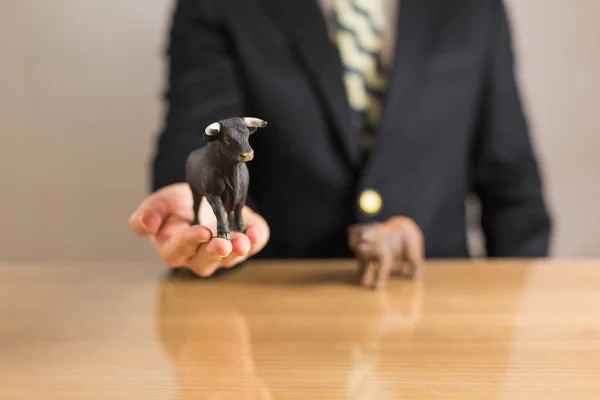 Young businessman trader holding in hands bear and bull figures. Bullish and Bearish market concept.