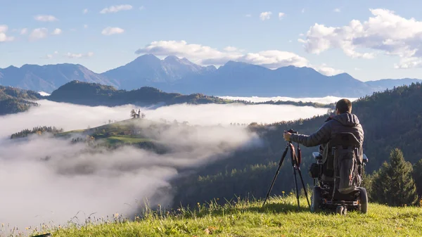 Mann im Rollstuhl fotografiert schöne Landschaft an einem nebligen Morgen, st. thomas slowenien — Stockfoto