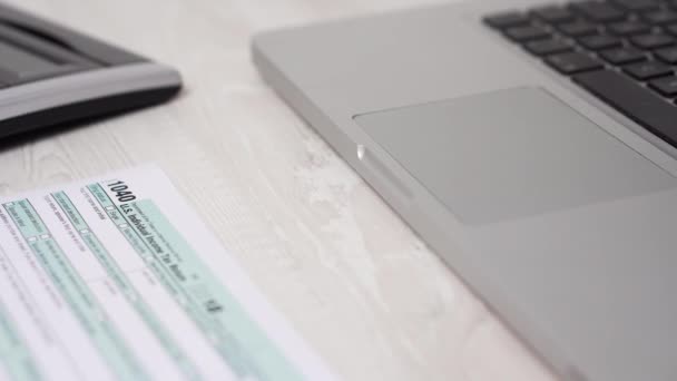 Снимок движения слайдера налоговой формы 1040 на столе рядом с ноутбуком и калькулятором. 4k видео — стоковое видео