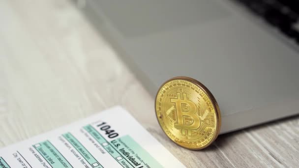 Slider shot of Bitcoin coin on the computer laptop next to 1040 Income Tax Return Refund Form concept. Bitcoins Y Dólares En La Mesa 4k video — Vídeos de Stock