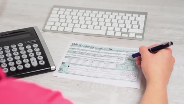 Por encima de la toma de hombro de la mujer que lee el formulario de impuestos 1040 y el cálculo de devolución de impuestos en el escritorio junto al teclado de la computadora y la calculadora. Vídeo 4k — Vídeo de stock